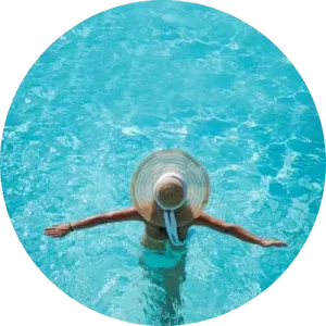 Person in sun hat swimming in pool with crystal clear water