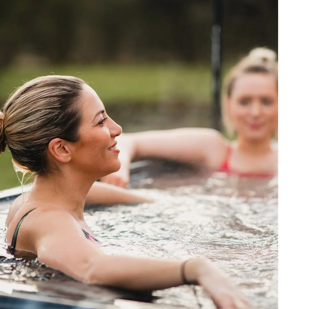 Two women sit in the swim spa together enjoying each other's company.