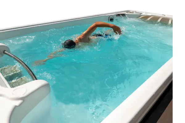 A man swims in a swim spa. He is wearing goggles and a swimcap.