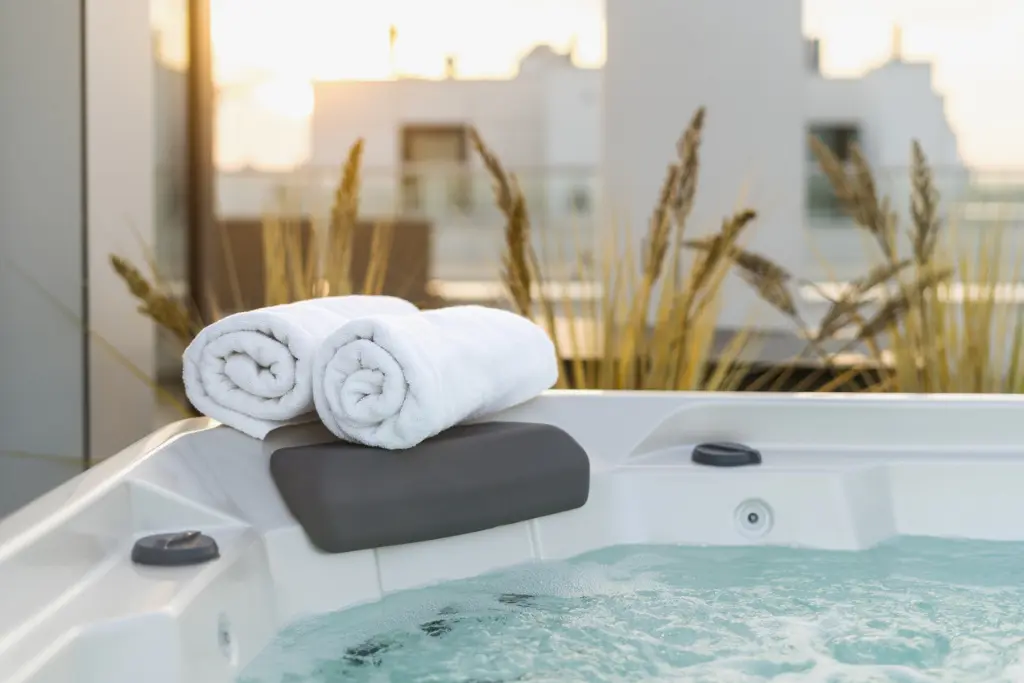 An outdoor hot tub in an industrial area. Three white towels rolled up sit on the edge of the spa.