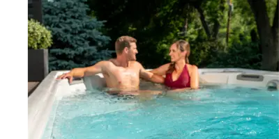 A couple relaxes in a swim spa together. They smile at each other.
