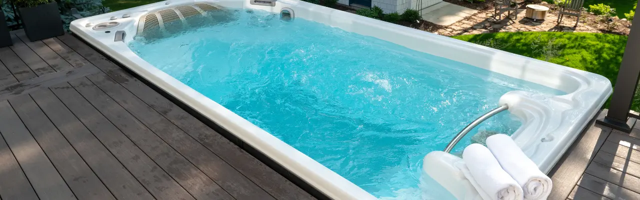 An overhead shot of a beautiful outdoor swim spa. It has 3 towels sitting on the edge of it.